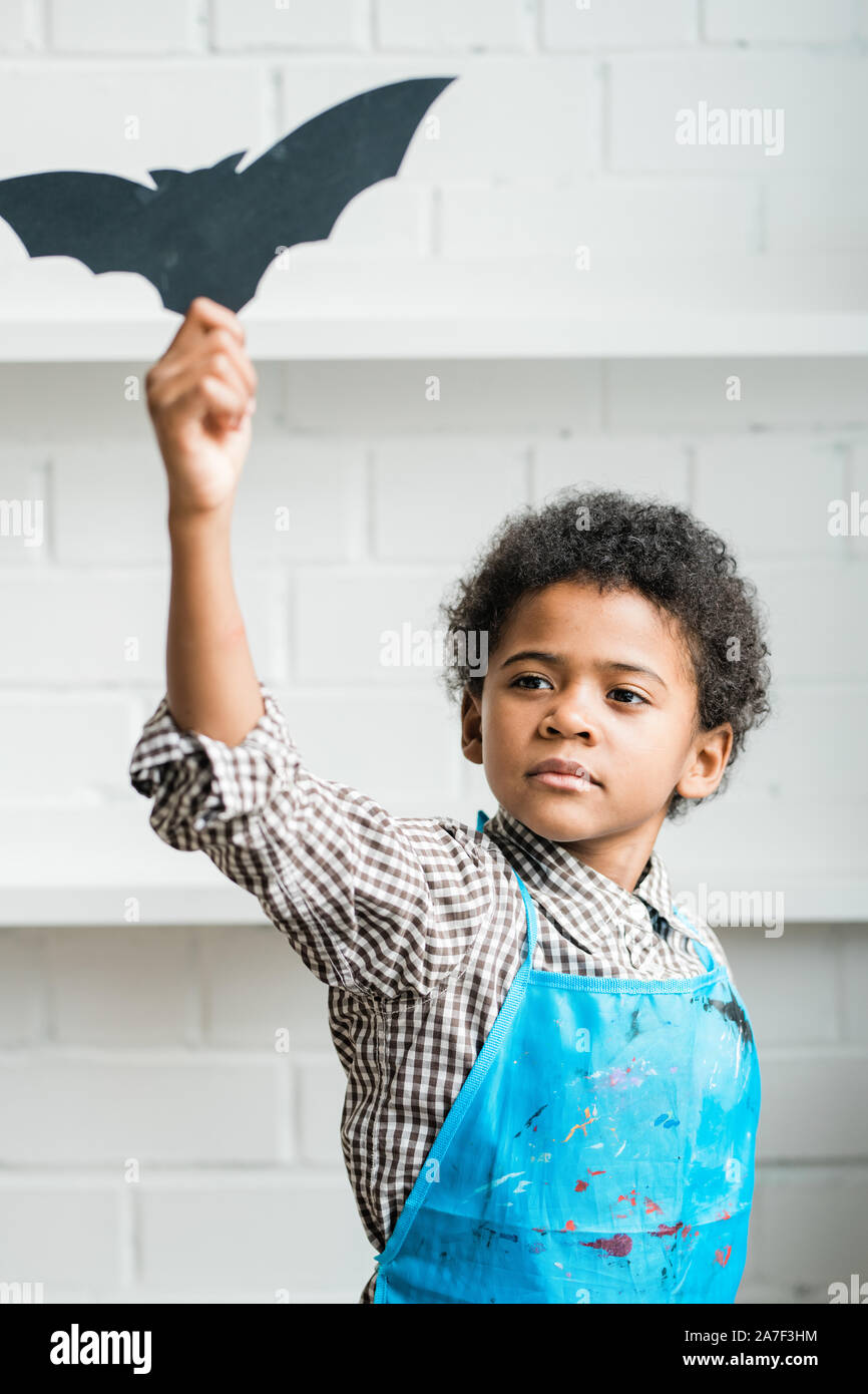African youngster in blue apron holding handmade halloween symbol Stock Photo
