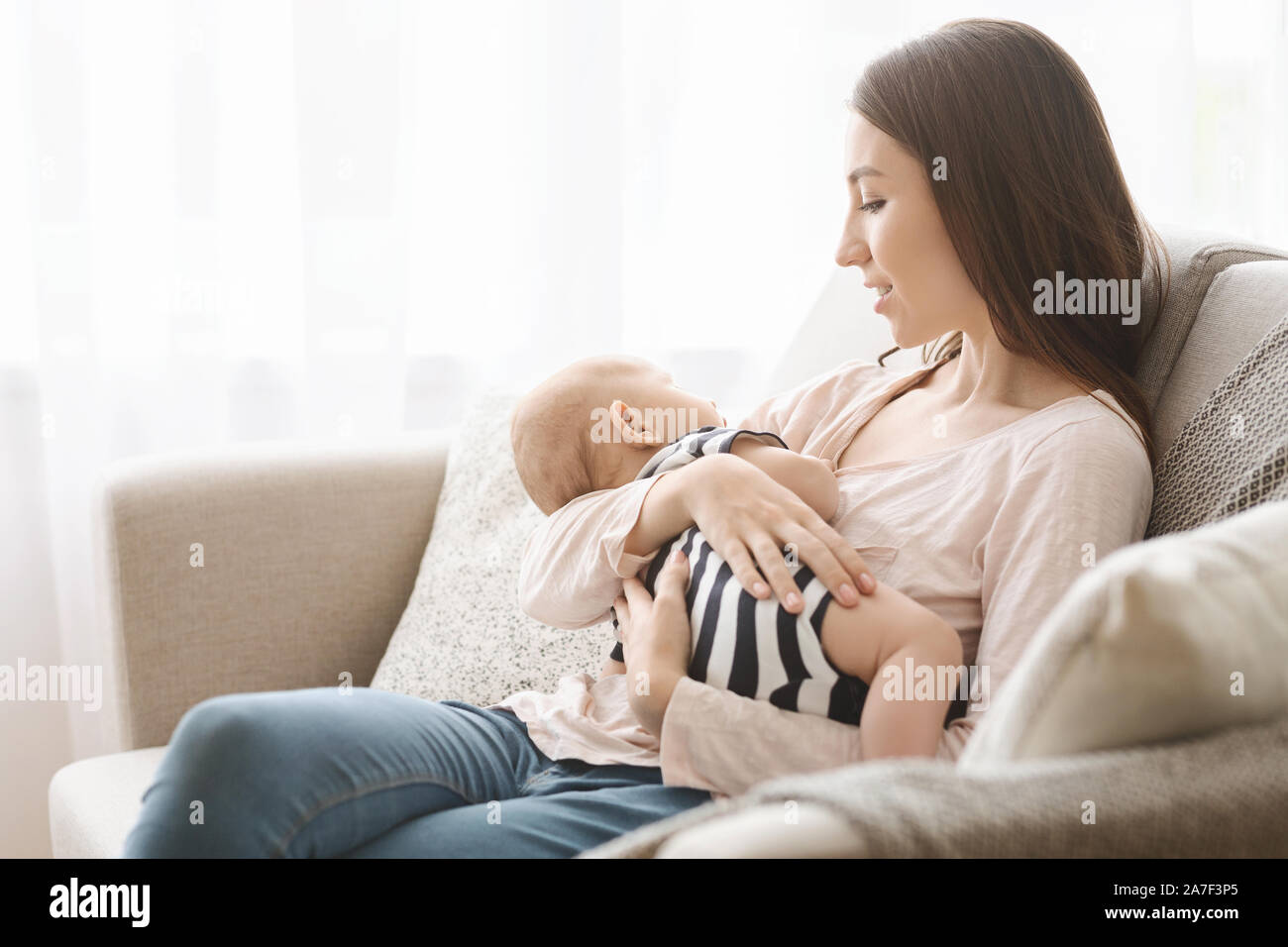Charming newborn baby fell asleep on mother's arms after breastfeeding Stock Photo