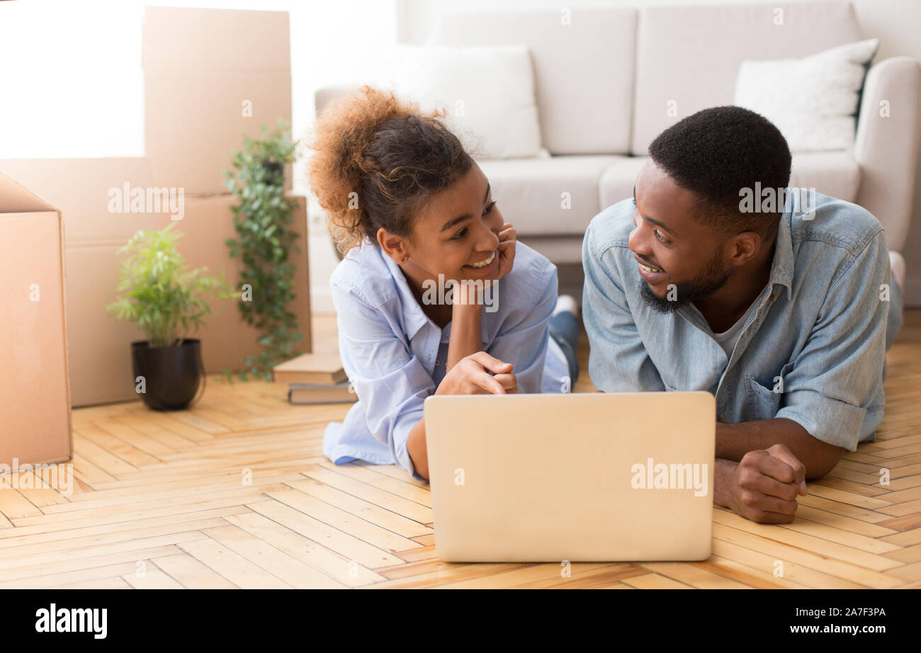 Spouses Using Laptop Lying On Floor Among Moving Boxes Indoor Stock Photo