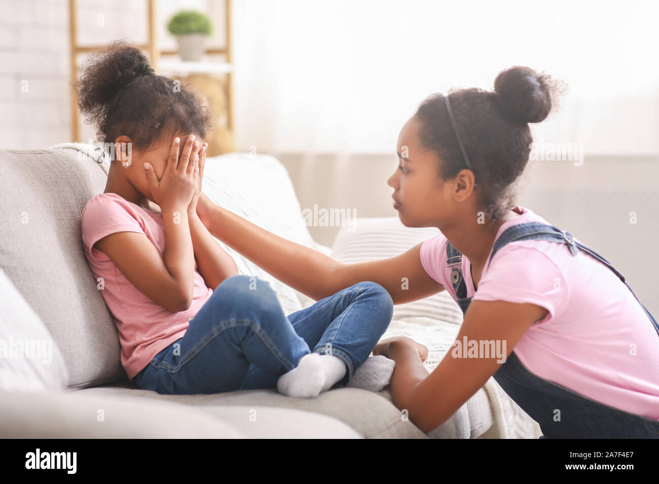 Caring african teen girl calming her sad crying baby sister Stock Photo