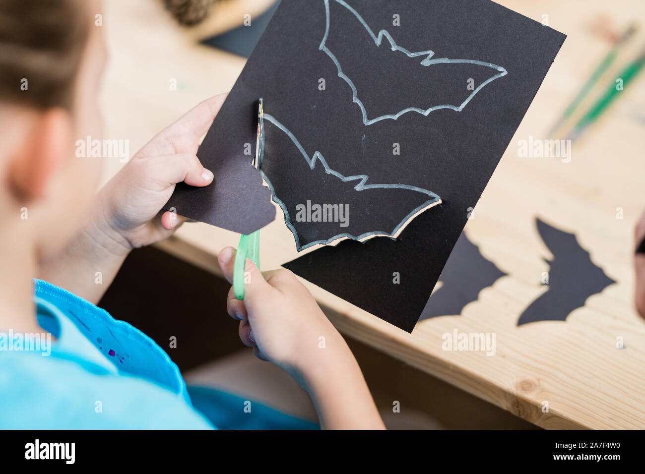 Hands of elementrary pupil cutting out halloween bat from black paper Stock Photo