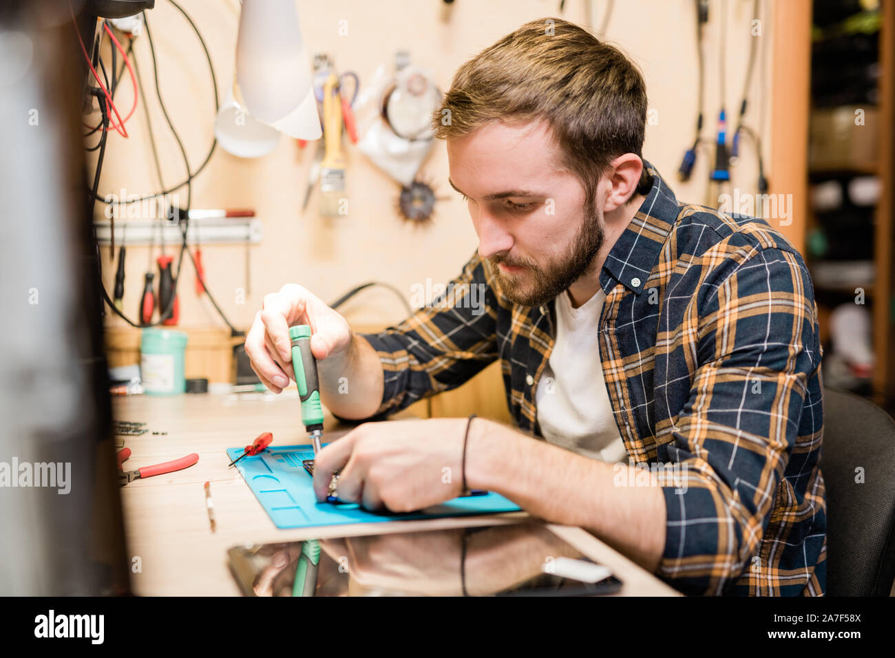 Serious repairman bending over broken gadget on table while using screwdriver Stock Photo