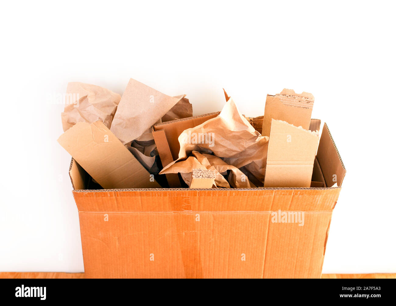 Cardboard box with crumpled paper and cardboard pieces against white wall. Close-up. Stock Photo