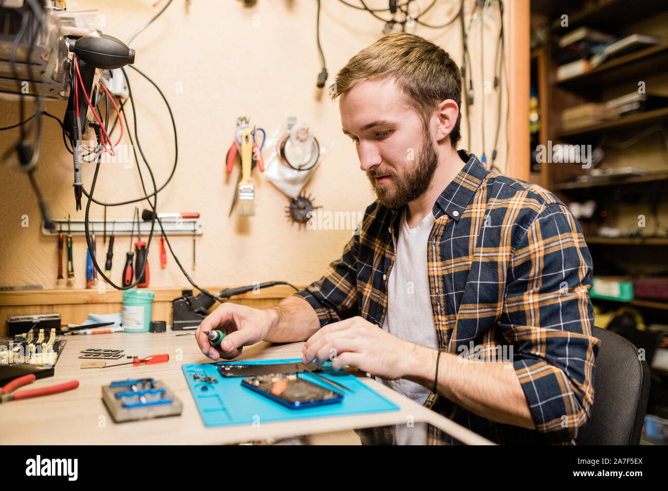 Professional repairman with screwdriver repairing broken smartphone in workshop Stock Photo