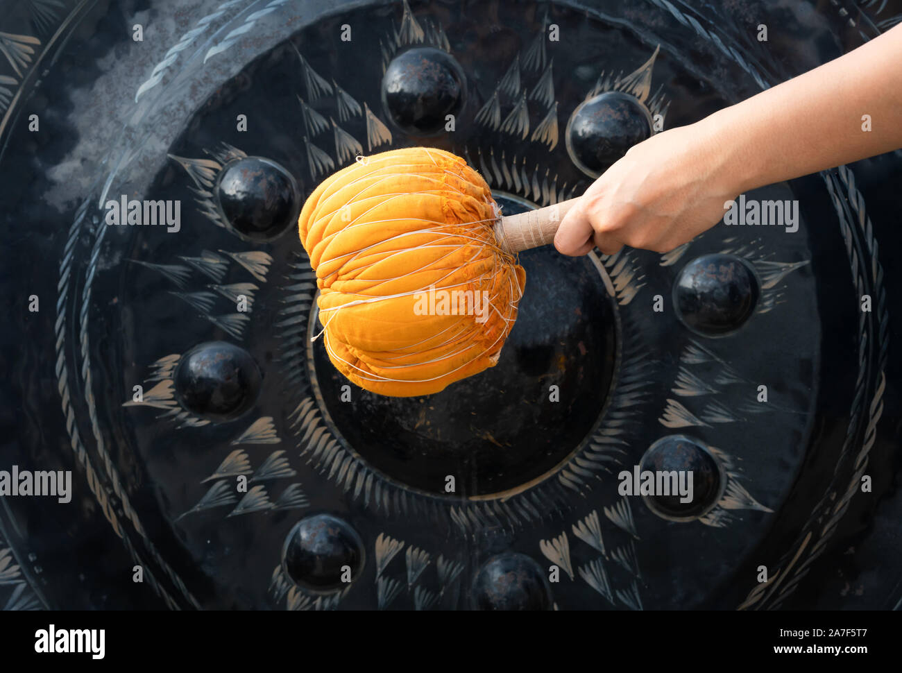 Hand striking a metal gong with an orange mallet at an asian buddhist