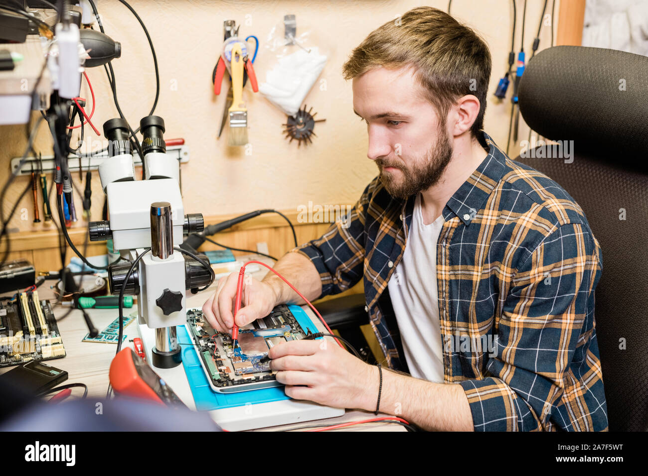 Young serious mechanic with two soldering-irons repairing demounted touchpad Stock Photo