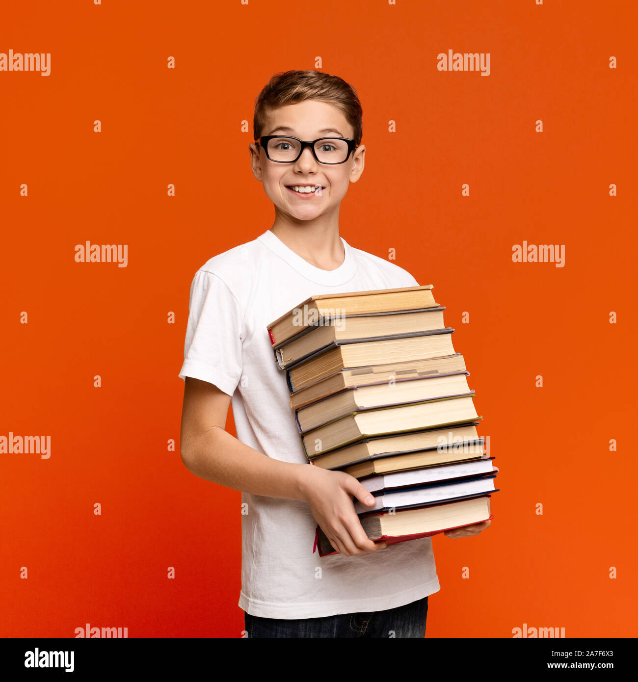 Smart teenage boy in glasses holding stack of books Stock Photo