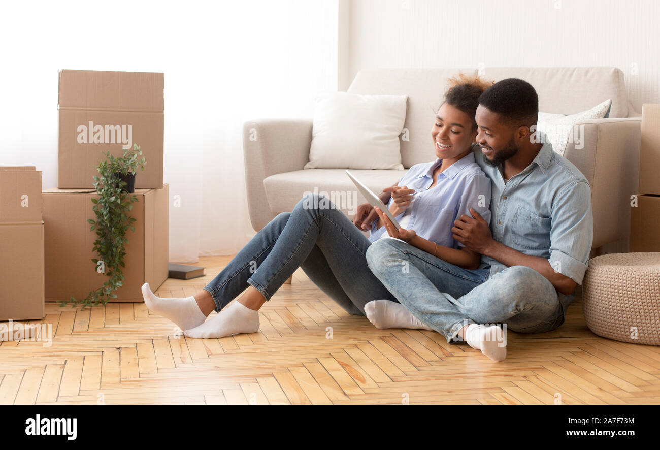 Spouses Using Tablet Sitting On Floor Among Unpacked Boxes Indoor Stock Photo