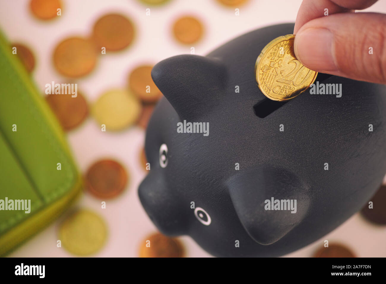 Person putting 20 euro cent coin into black piggy bank. Close up. Stock Photo