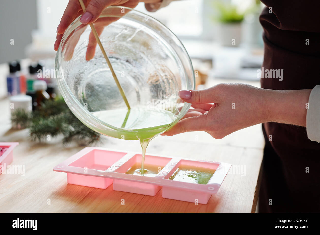 Girl pouring liquid soap mass with green color into pink silicone molds Stock Photo