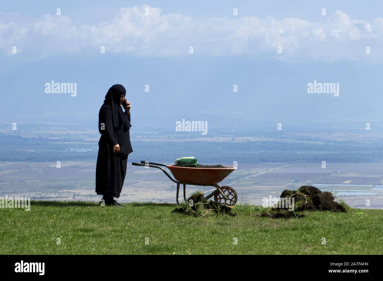 Georgia, 2019: old nun during gardening reaches for mobile phone - Bodbe monastery Stock Photo