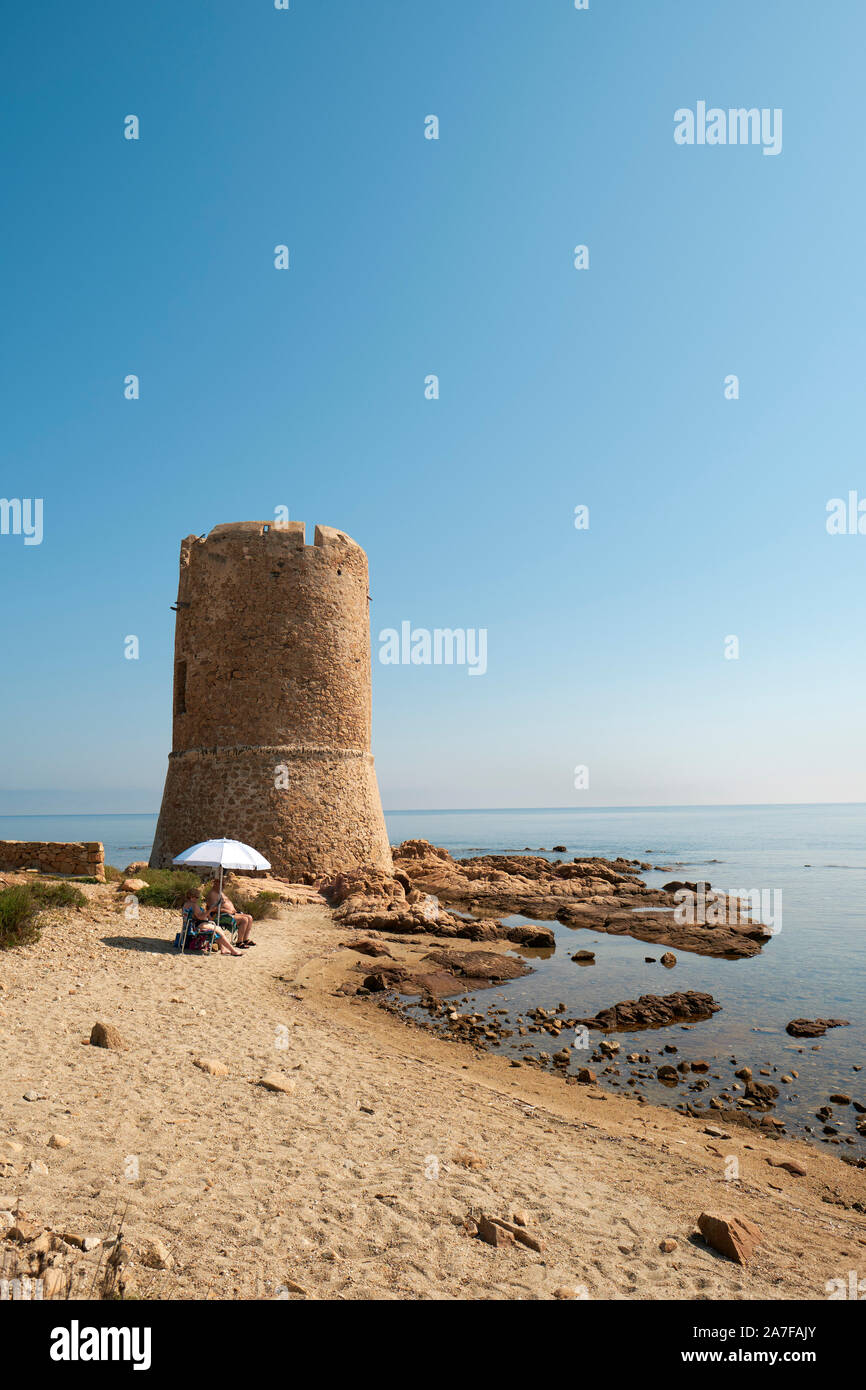 A small summer beach with a parasol and the Torre di San Giovanni watchtower on the Sardinian coast at La Caletta in Nuoro Sardinia Italy Europe Stock Photo