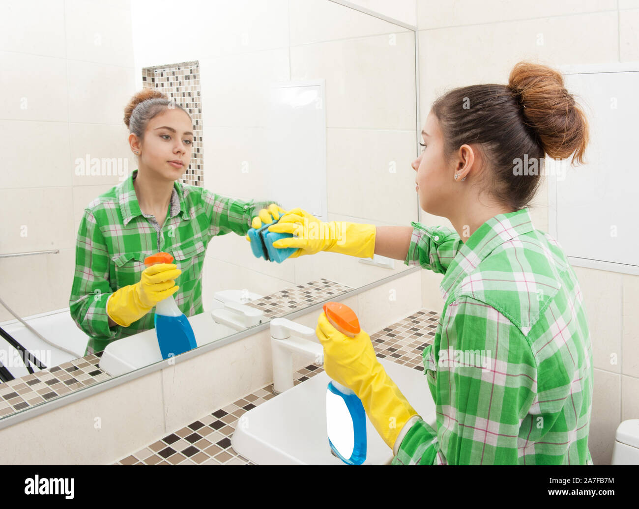 Gloved housewife washes a mirror in the bathroom Stock Photo