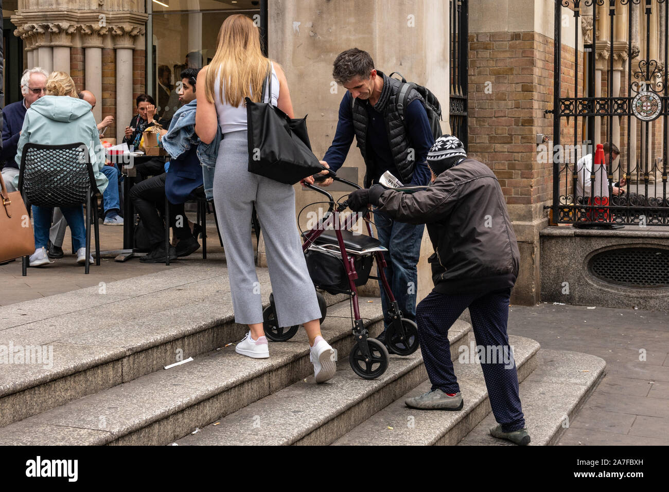 An elderly lady is helped climb the steps to Liverpool Street Station by kind hearted passers by. London UK Stock Photo