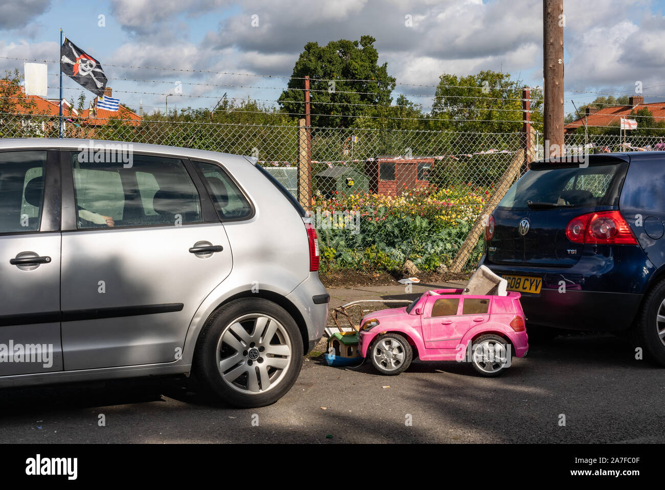 A dumped Childs toy car is sitting between two hatchback cars on the Watling Estate in North London UK Stock Photo