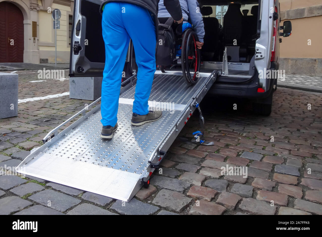 Assistant helping disabled person on wheelchair with transport using