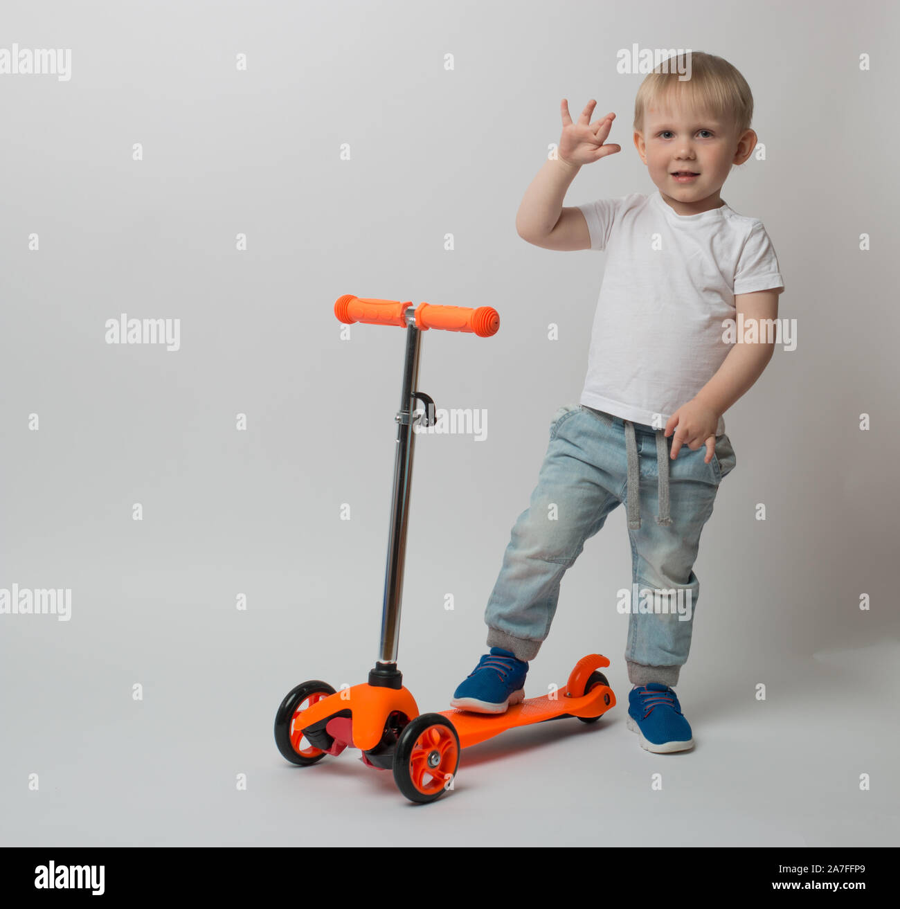 Toddler, a very joyful child, raised his hand stay on the scooter's . Concept for advertising and articles about toys and bicycles on a white backgrou Stock Photo