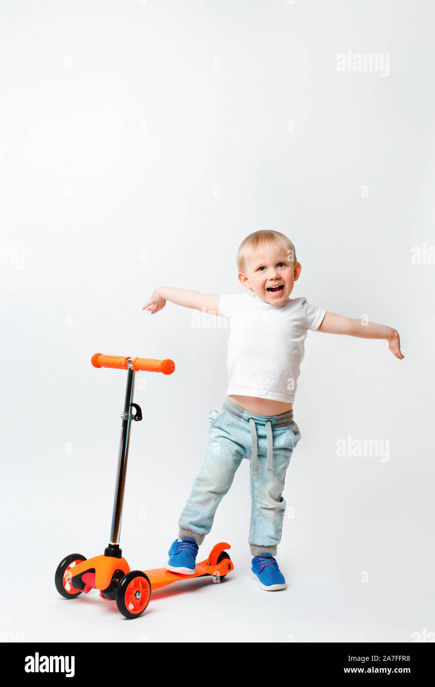 Toddler, a very joyful child, raised his hands in awe of the scooter's gift. Concept for advertising and articles about toys and bicycles on a white b Stock Photo