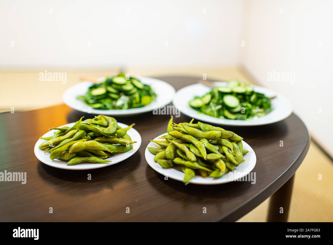 Traditional home room with wooden table and green salad dish with Japanese cucumbers and mizuna greens and boiled edamame soy beans Stock Photo