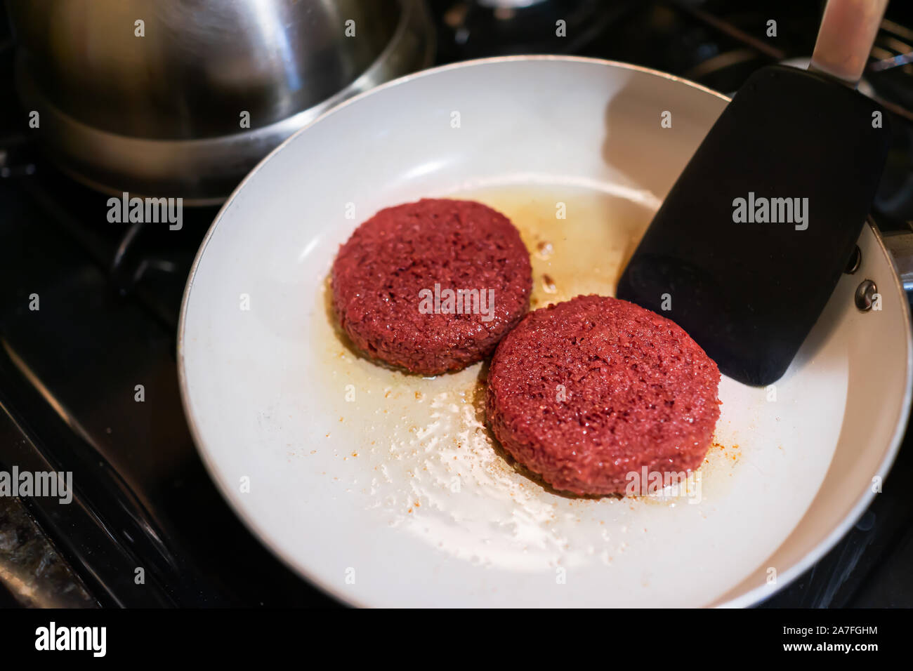 Closeup of two raw vegan meat sausage patties cooking on ceramic nonstick frying pan with oil grease spatula flipping Stock Photo