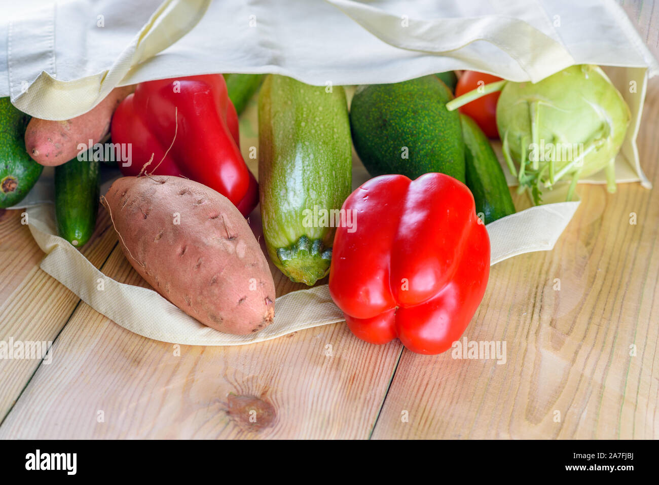 World free of plastic.Reusable eco friendly canvas grocery shopping bag with vegetables-sweet potato, zucchini, pepper, tomatoes, cucumber and avocado on wooden desk. Organic products. Less plastic. Stock Photo