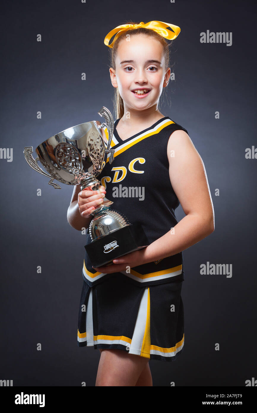 A young Caucasian girl dressed in a Cheer Dance outfit and holding a trophy. England, UK. Stock Photo