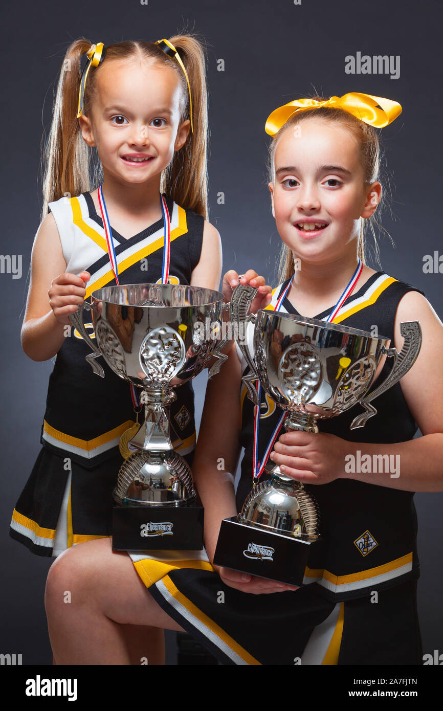 Two young Caucasian girls dressed in Cheer Dance outfits and holding a trophy. England, UK. Stock Photo