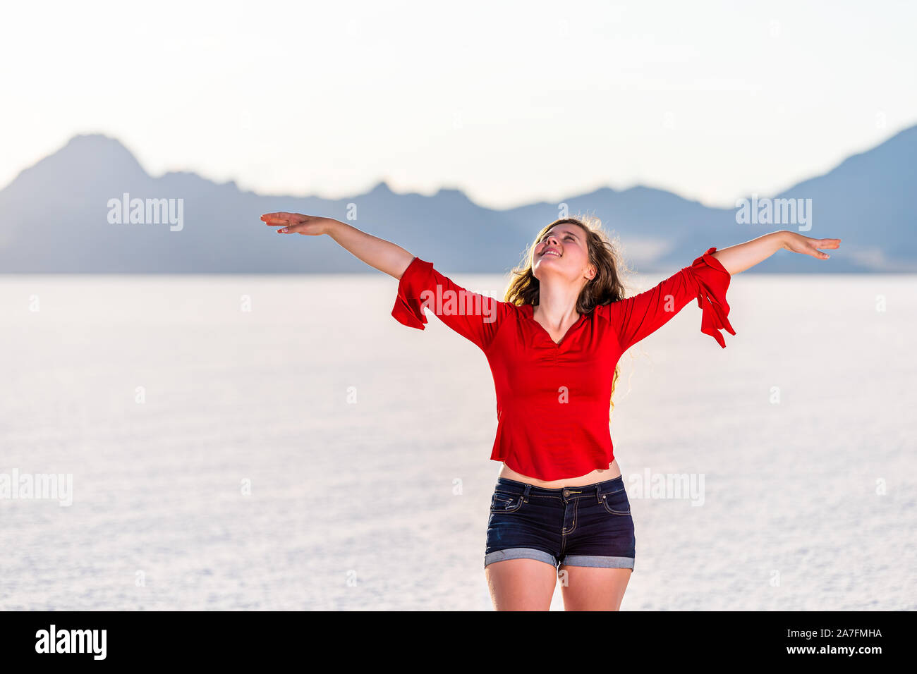 Young happy woman with hands raised up on white Bonneville Salt Flats near Salt Lake City, Utah and mountain view during sunset Stock Photo