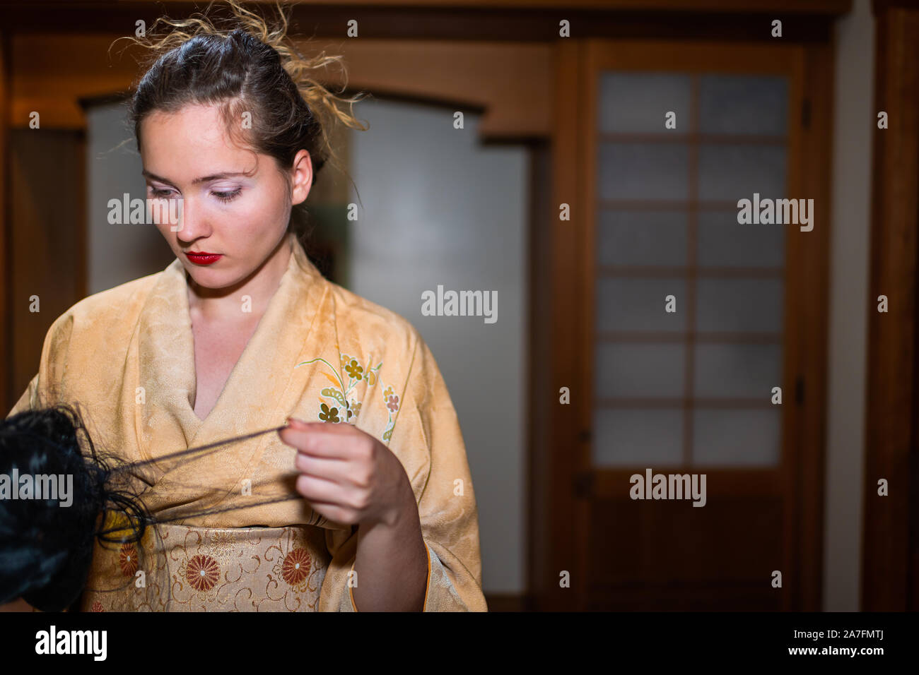 Young woman in kimono getting ready by traditional wooden door holding black wig in Japanese house home Stock Photo