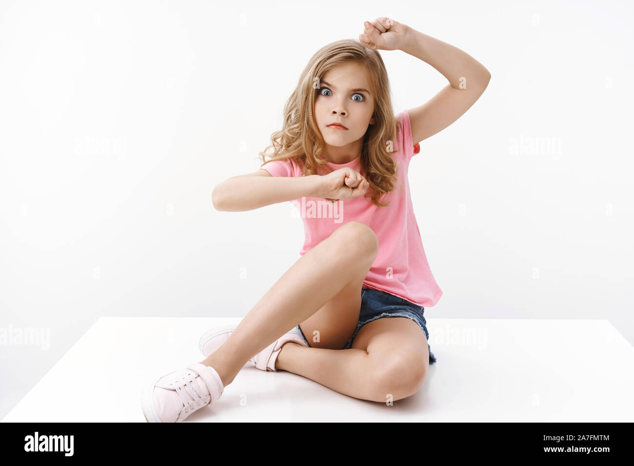 Playful funny pretty teenage blond girl, sit on floor, making serious grimace, stare camera shake raised hands, wanna scare with glance, fool around Stock Photo