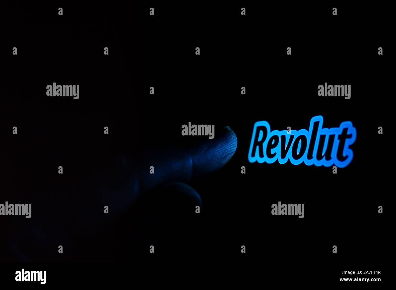 Revolut bank logo on a smartphone screen in a dark room and a finger touching it. Stock Photo