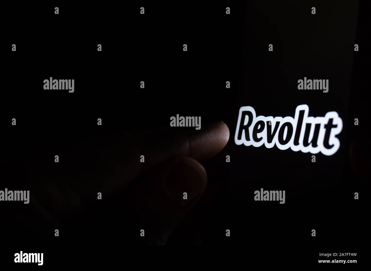 Revolut bank logo on a smartphone screen in a dark room and a finger touching it. Stock Photo