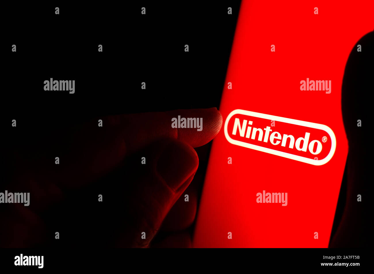 Nintendo logo on a red smartphone screen in a dark room and a finger touching it. Stock Photo