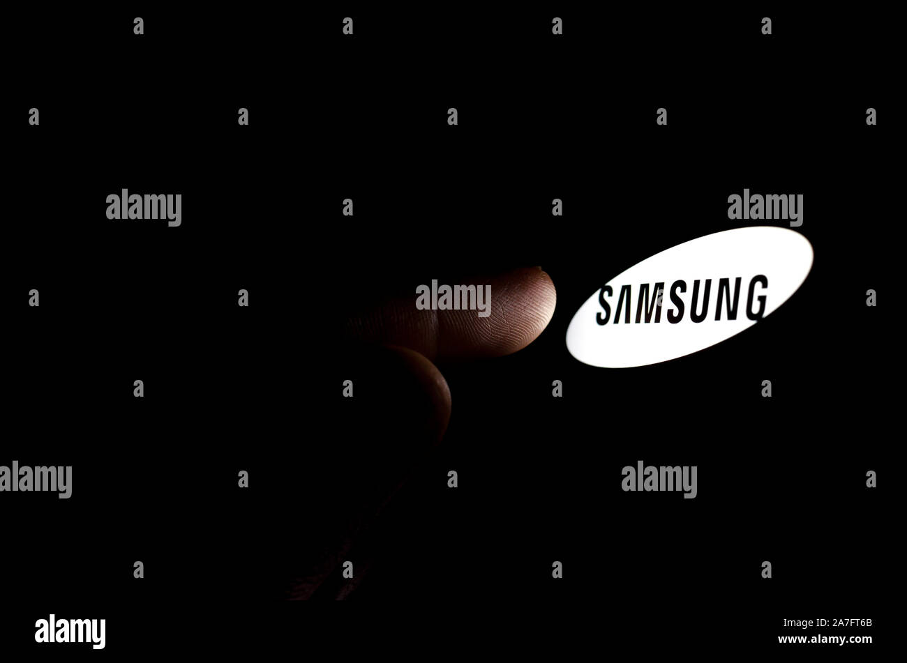 Samsung logo on a smartphone screen in a dark room and a finger touching it. Stock Photo