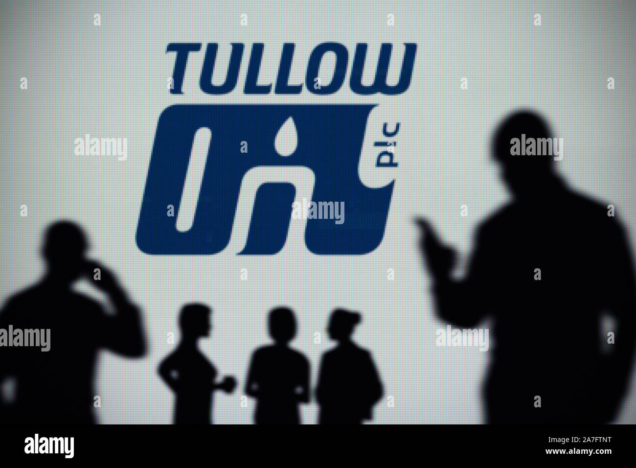 The Tullow Oil logo is seen on an LED screen in the background while a silhouetted person uses a smartphone (Editorial use only) Stock Photo