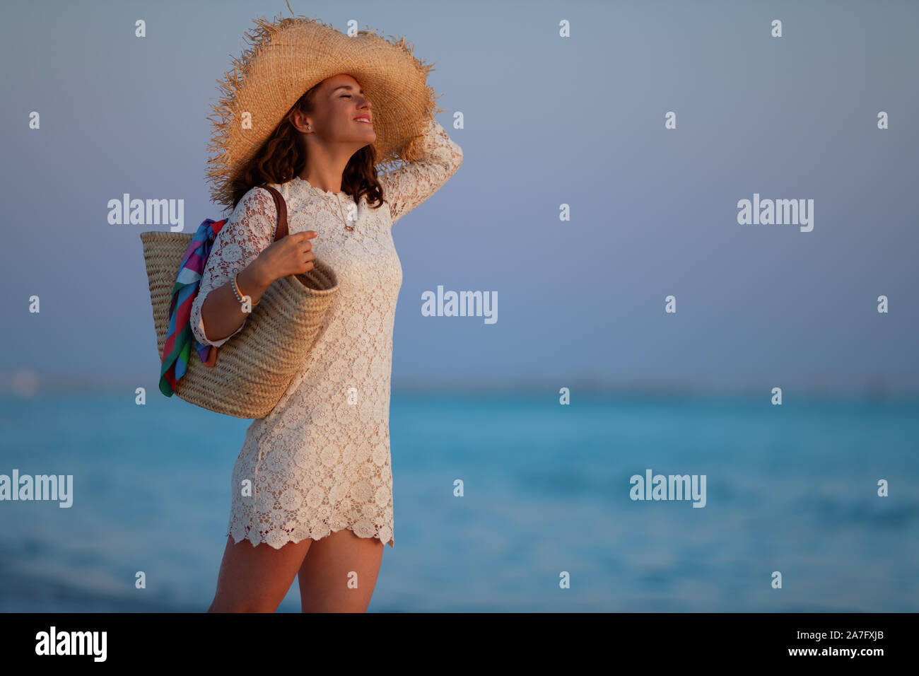 Side view of happy young woman in white dress and straw hat on the ...