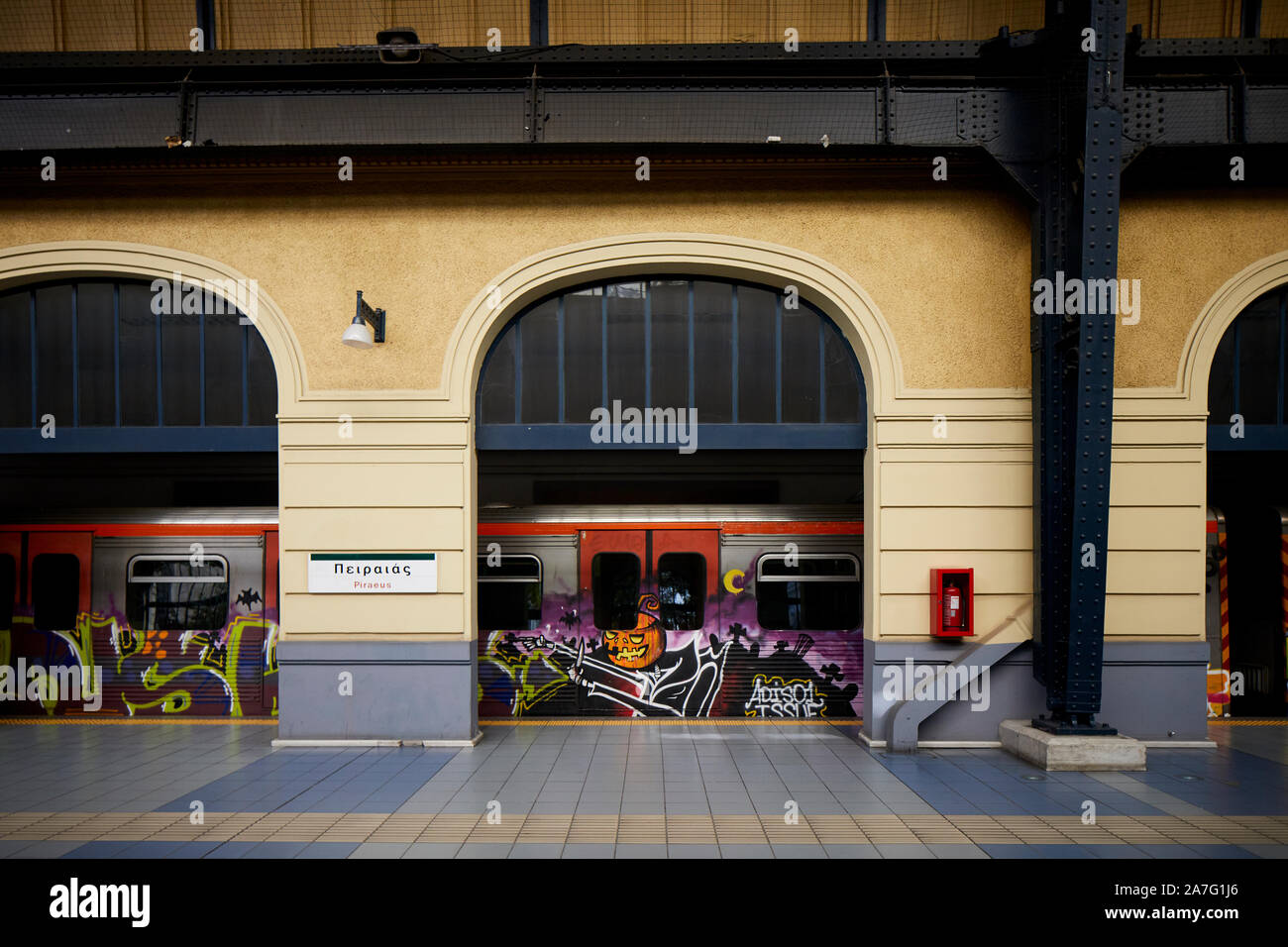 Piraeus port city Greece underground metro terminus of Athens Metro Line 1 a graffiti covers train departs under he ornate station shed roof Stock Photo