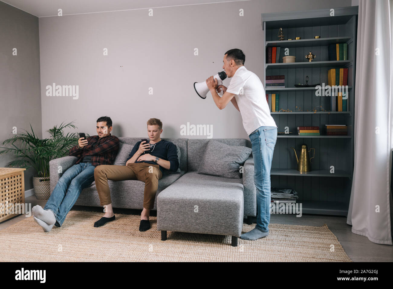 Young man yelling through megaphone at friends which using a mobile phone. Stock Photo