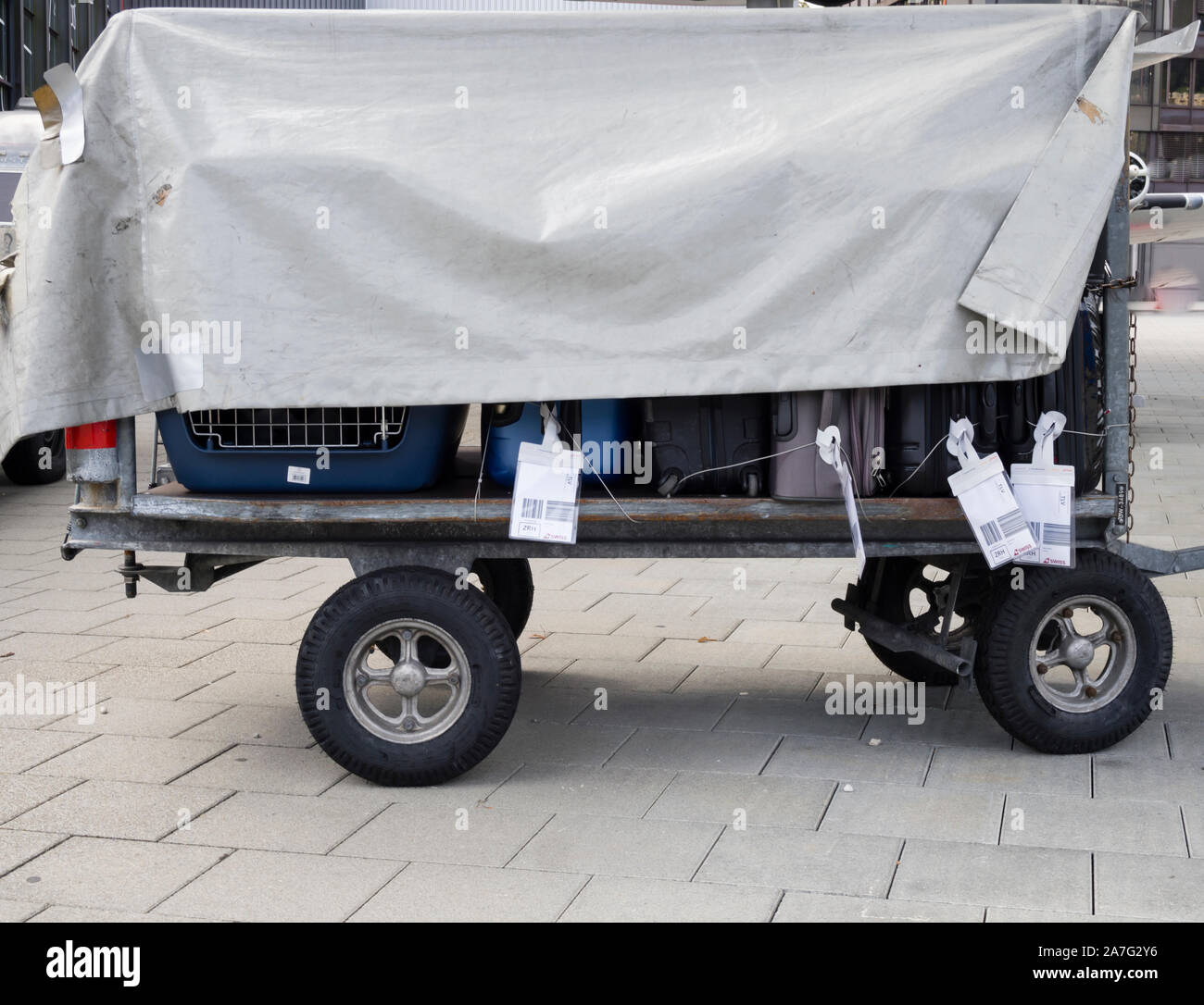 Airport luggage cart loaded with suitcases outside on an airfield. Suitcases only partially visible under tarpaulin. Stock Photo