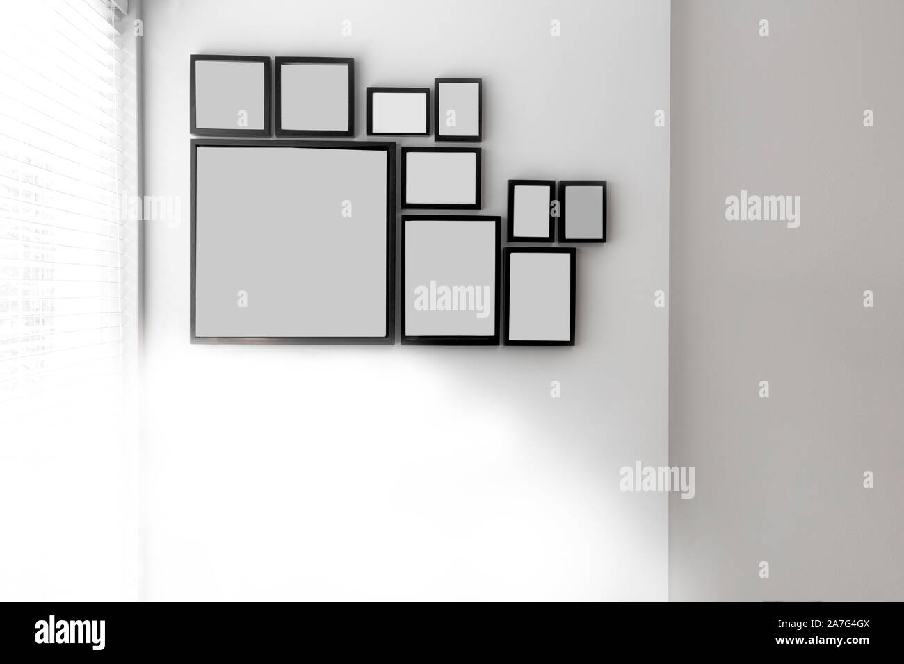 Group of various blank black picture frames on grey wall near a window