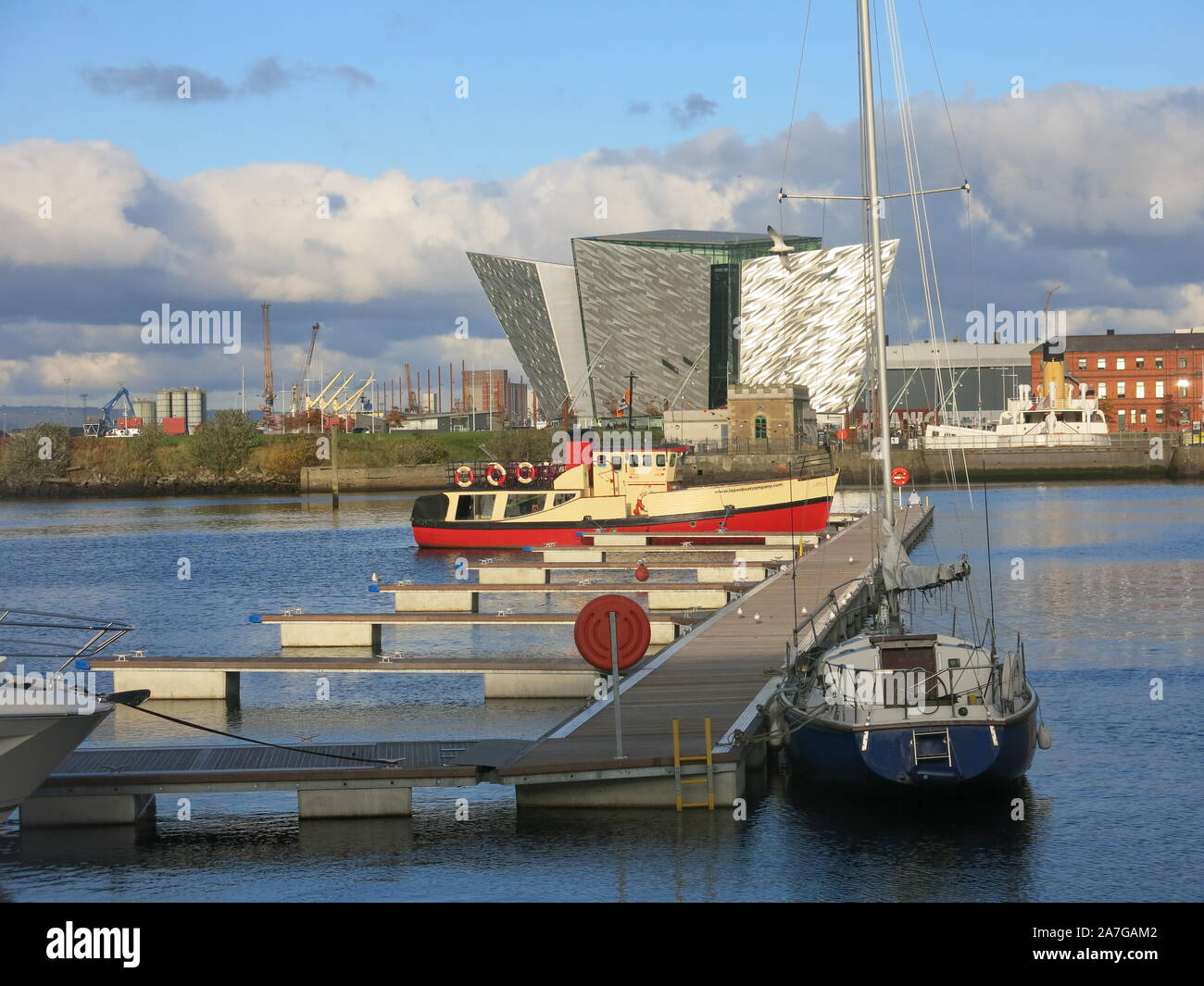 View of boats moored by a jetty in the regenerated waterfront Titanic Quarter in central Belfast, the Titanic Museum in the background. Stock Photo