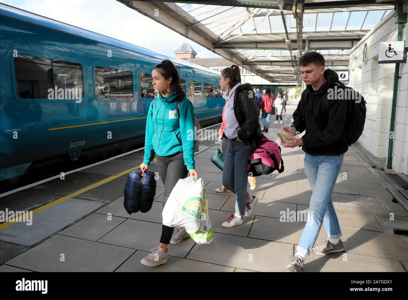 Young people women students with rucksacks and bags getting on KeolisAmey run train at Bangor railway station in Gwynedd North Wales UK  KATHY DEWITT Stock Photo