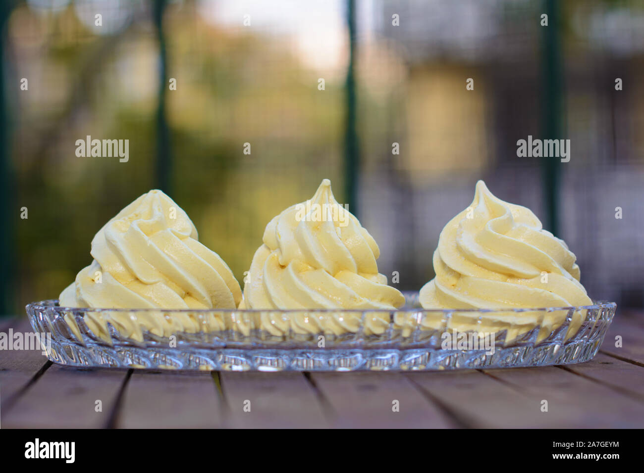 Three yellowish meringues in a glass cake plate Stock Photo Alamy