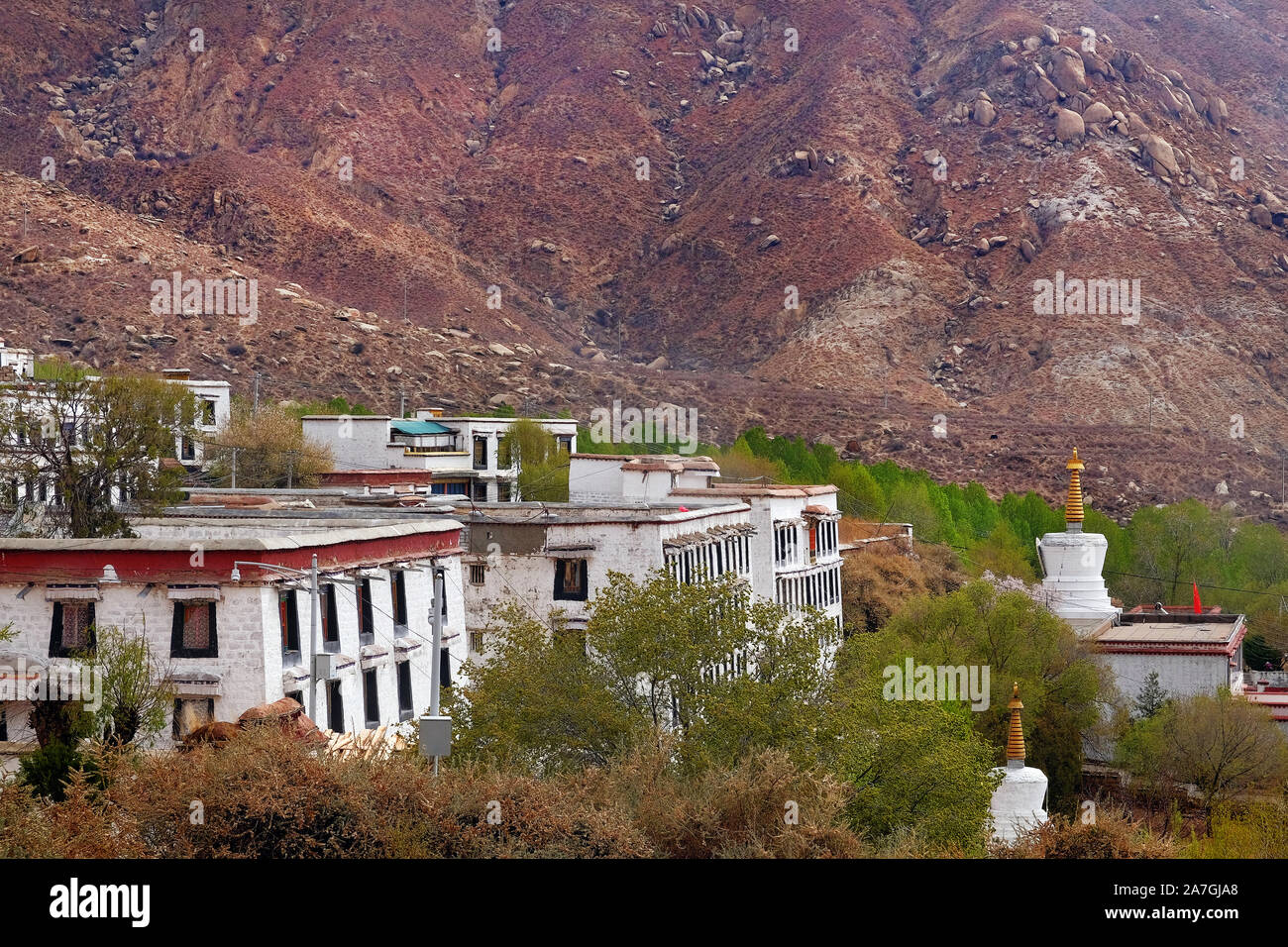 View of brown colored mountains surrounding the white walls of the Drepung Monastery in Lhasa, Tibet. Stock Photo