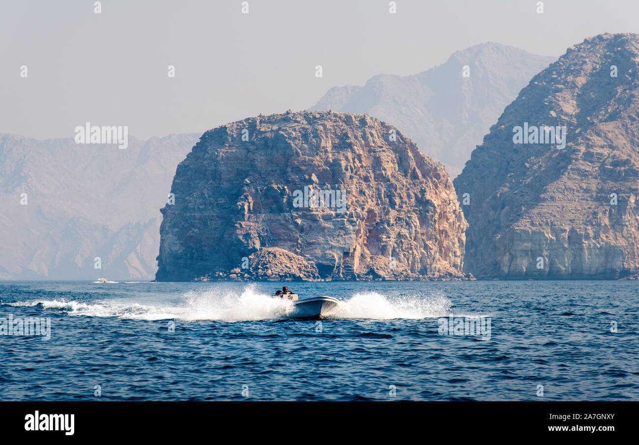 Boat floating on seaside surrounded by desert rocks near Khasab, Musandam Oman Stock Photo