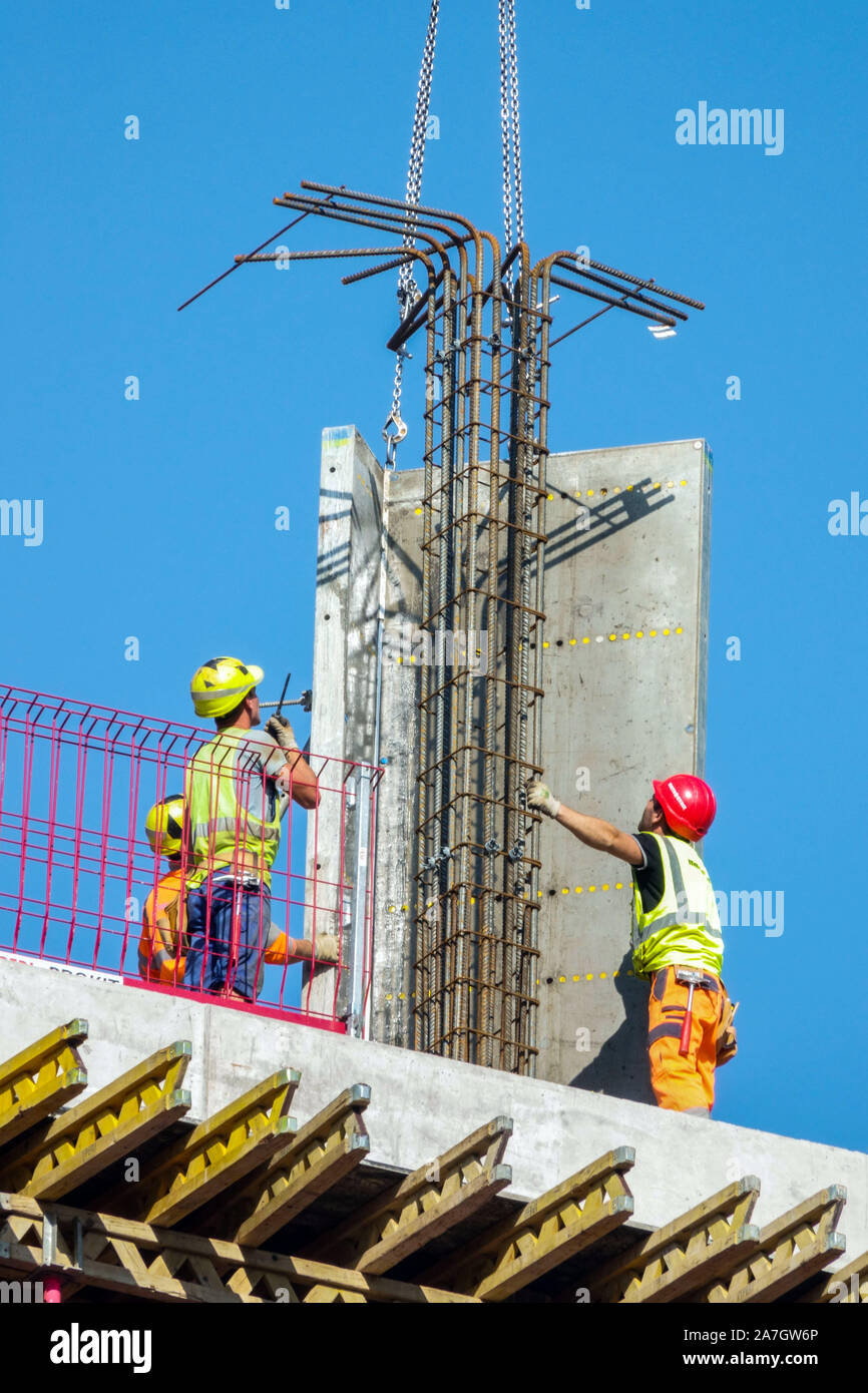 Three construction workers are precisely settling the concrete block by crane Stock Photo