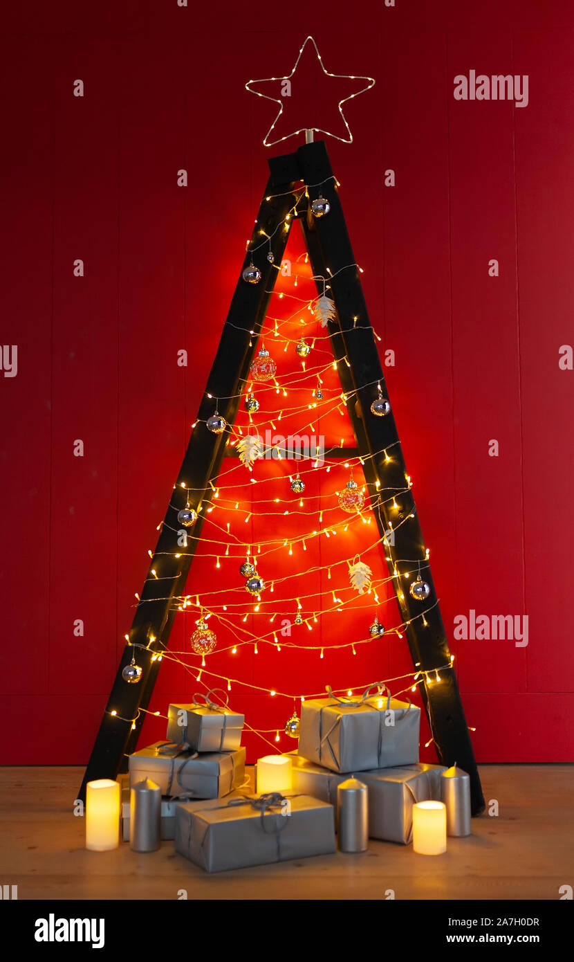 Scandinavian style Christmas tree. Made of a step ladder and decorated with lights and garlands on red background. Stock Photo