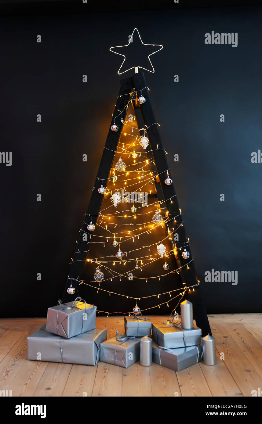 Scandinavian style Christmas tree. Made of a step ladder and decorated with lights and garlands on black background. Stock Photo
