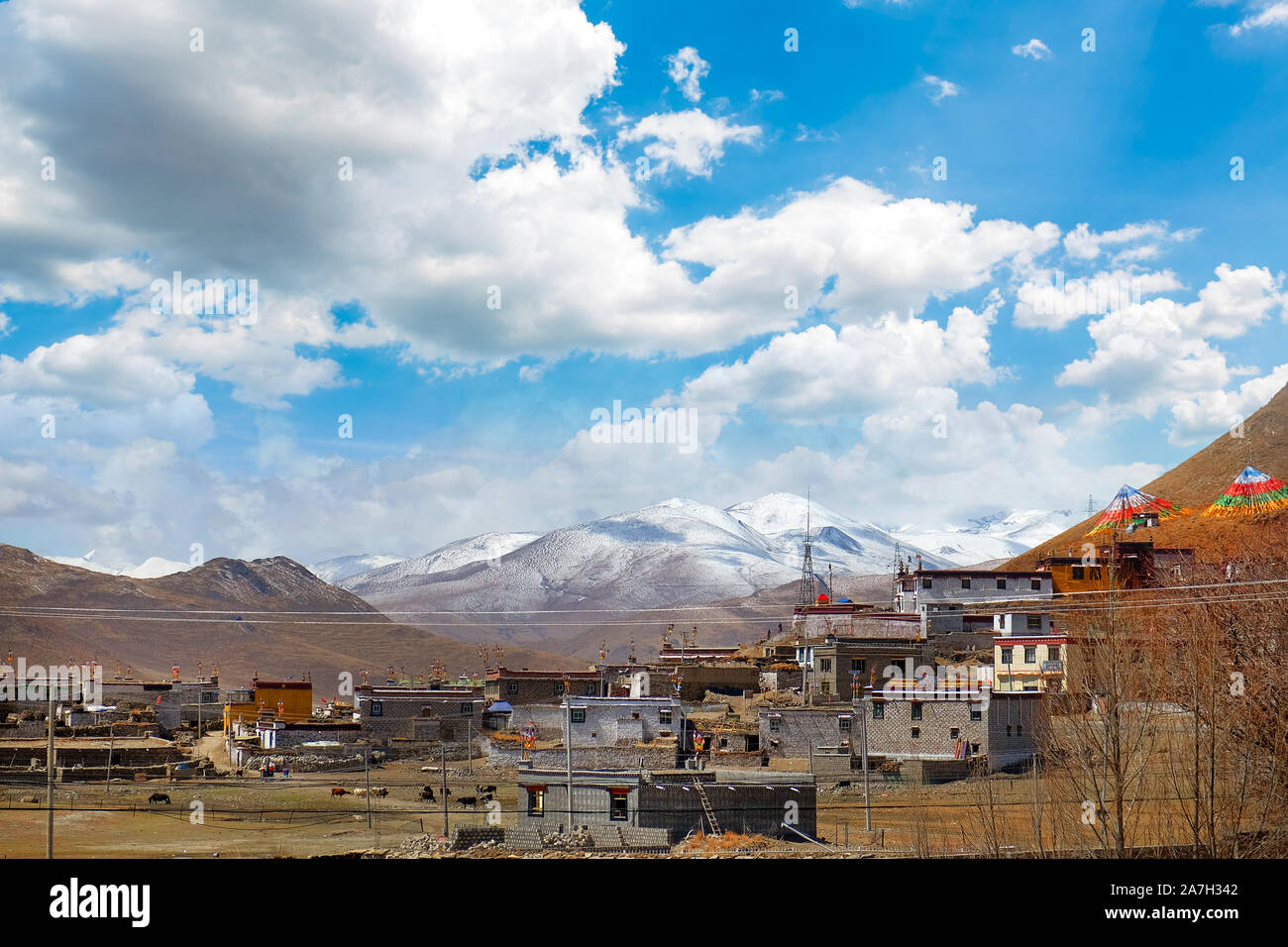 View of traditional Tibetan village against the Himalayan Mountains, against a blue sky covered by white clouds. Stock Photo