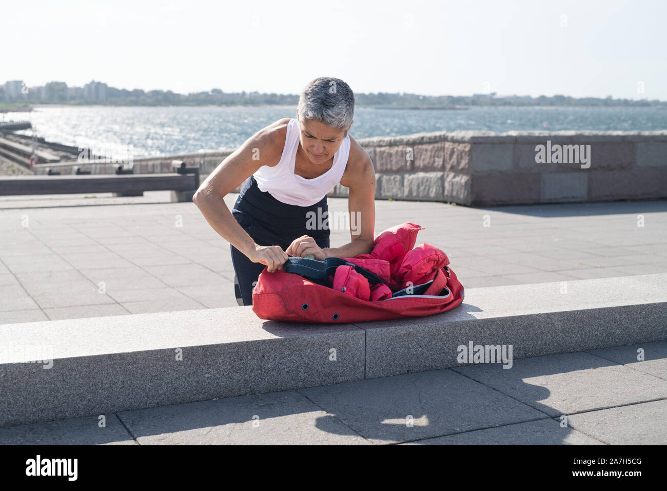 Middle-aged woman packing up yoga gear by ocean Stock Photo